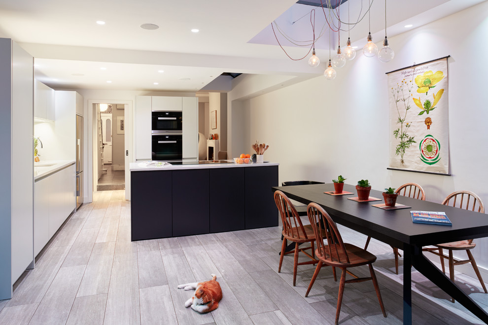 This is an example of a large contemporary single-wall eat-in kitchen in London with a drop-in sink, flat-panel cabinets, white cabinets, solid surface benchtops, blue splashback, glass tile splashback, panelled appliances, porcelain floors and with island.