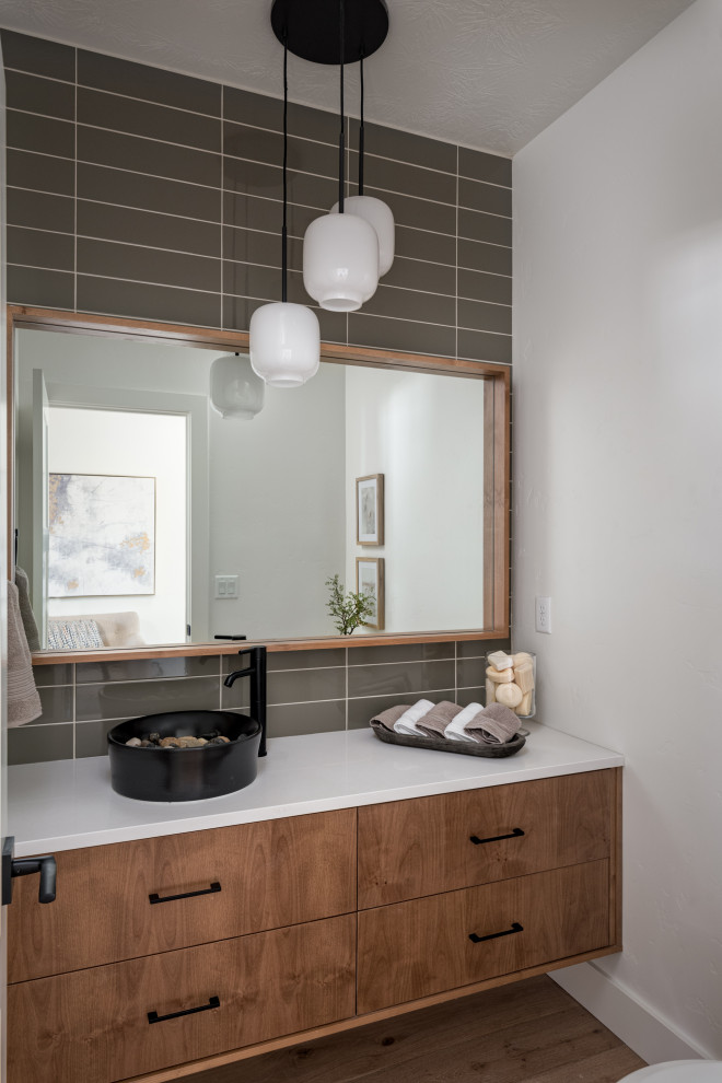 Design ideas for a transitional powder room in Boise with flat-panel cabinets, medium wood cabinets, gray tile, white walls, medium hardwood floors, a vessel sink, brown floor and white benchtops.