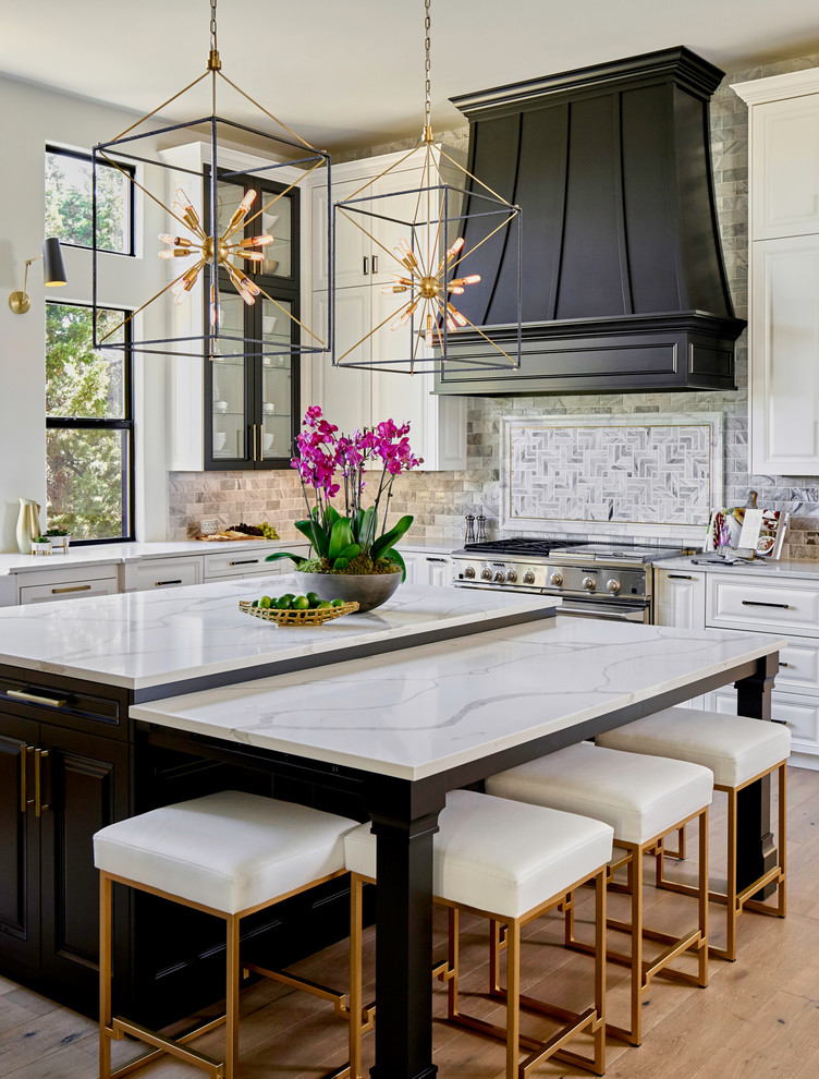 Design ideas for a large traditional l-shaped kitchen in Austin with white cabinets, quartz benchtops, marble splashback, stainless steel appliances, light hardwood floors, with island, white benchtop and raised-panel cabinets.