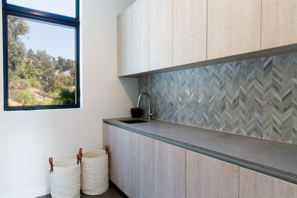 This is an example of a large modern galley dedicated laundry room in Los Angeles with flat-panel cabinets, light wood cabinets, concrete benchtops, grey walls, ceramic floors, a side-by-side washer and dryer, grey floor and grey benchtop.