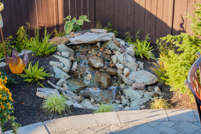 This is an example of a mid-sized rustic full sun backyard stone water fountain landscape in Seattle for spring.