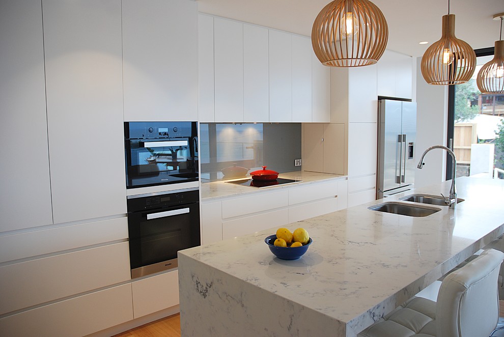 This is an example of a large contemporary single-wall eat-in kitchen in Sydney with an undermount sink, flat-panel cabinets, white cabinets, quartz benchtops, blue splashback, glass sheet splashback, black appliances, medium hardwood floors and with island.