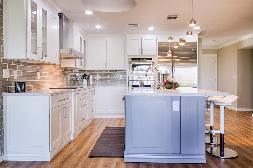 Open concept kitchen - mid-sized transitional l-shaped laminate floor open concept kitchen idea in Phoenix with an undermount sink, shaker cabinets, white cabinets, quartzite countertops, gray backsplash, ceramic backsplash, stainless steel appliances and an island