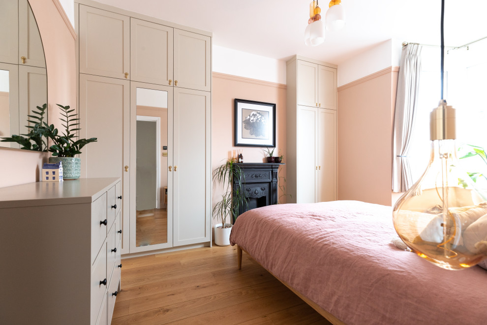 This is an example of a medium sized contemporary master and grey and pink bedroom in London with pink walls, medium hardwood flooring, a standard fireplace, brown floors and feature lighting.