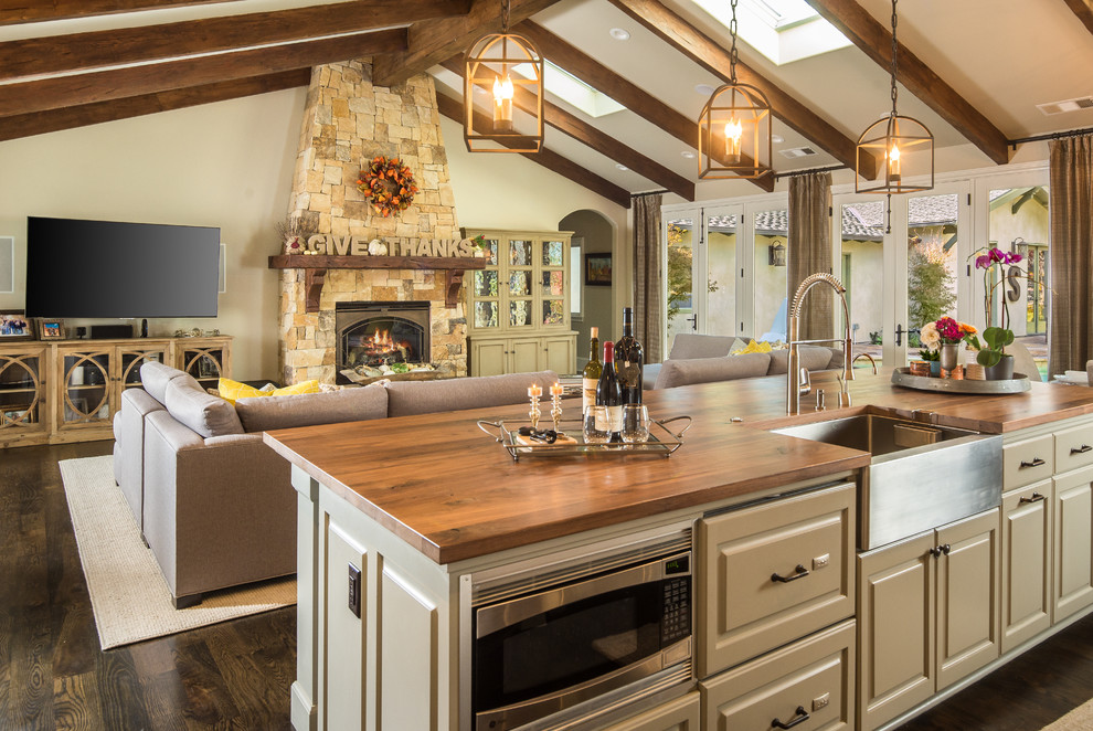 Open concept kitchen - large transitional single-wall dark wood floor and brown floor open concept kitchen idea with a farmhouse sink, raised-panel cabinets, gray cabinets, wood countertops, beige backsplash, stone tile backsplash, stainless steel appliances and an island