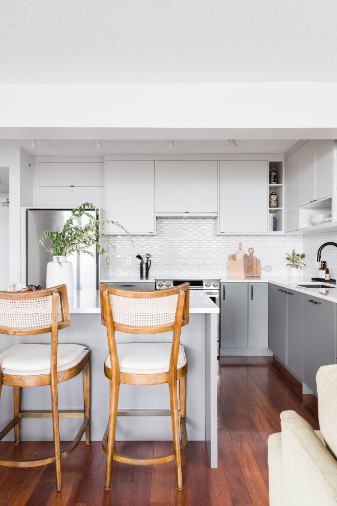 Photo of a mid-sized contemporary l-shaped eat-in kitchen in Vancouver with an undermount sink, shaker cabinets, white cabinets, quartz benchtops, white splashback, porcelain splashback, stainless steel appliances, medium hardwood floors, with island, brown floor and white benchtop.