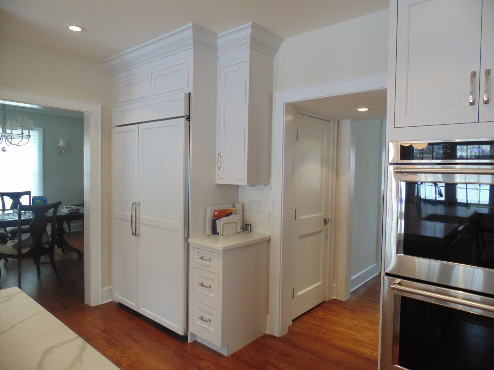 Example of a large transitional u-shaped medium tone wood floor and brown floor eat-in kitchen design with a farmhouse sink, recessed-panel cabinets, white cabinets, quartz countertops, white backsplash, subway tile backsplash, stainless steel appliances, an island and white countertops