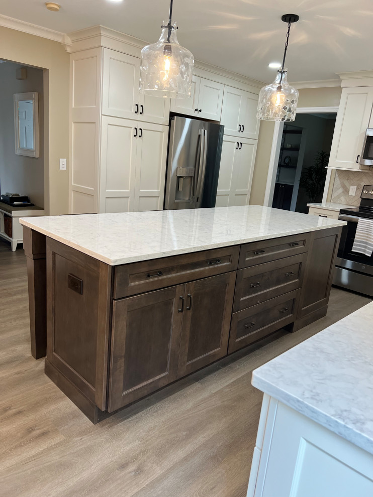 Example of a mid-sized transitional l-shaped laminate floor and brown floor kitchen pantry design in Cincinnati with an undermount sink, recessed-panel cabinets, white cabinets, quartz countertops, gray backsplash, stone tile backsplash, stainless steel appliances, an island and white countertops