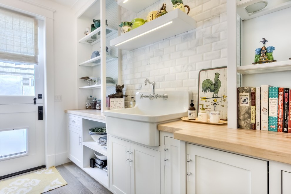 Photo of a large country galley kitchen pantry in Orange County with a farmhouse sink, white splashback, subway tile splashback, recessed-panel cabinets, white cabinets, wood benchtops and light hardwood floors.