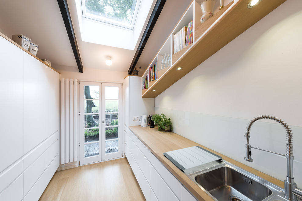 Geschlossene, Einzeilige, Mittelgroße Moderne Küche ohne Insel mit Einbauwaschbecken, Kassettenfronten, weißen Schränken, Arbeitsplatte aus Holz, Küchenrückwand in Weiß, Glasrückwand, weißen Elektrogeräten, hellem Holzboden, beigem Boden und beiger Arbeitsplatte in Sonstige