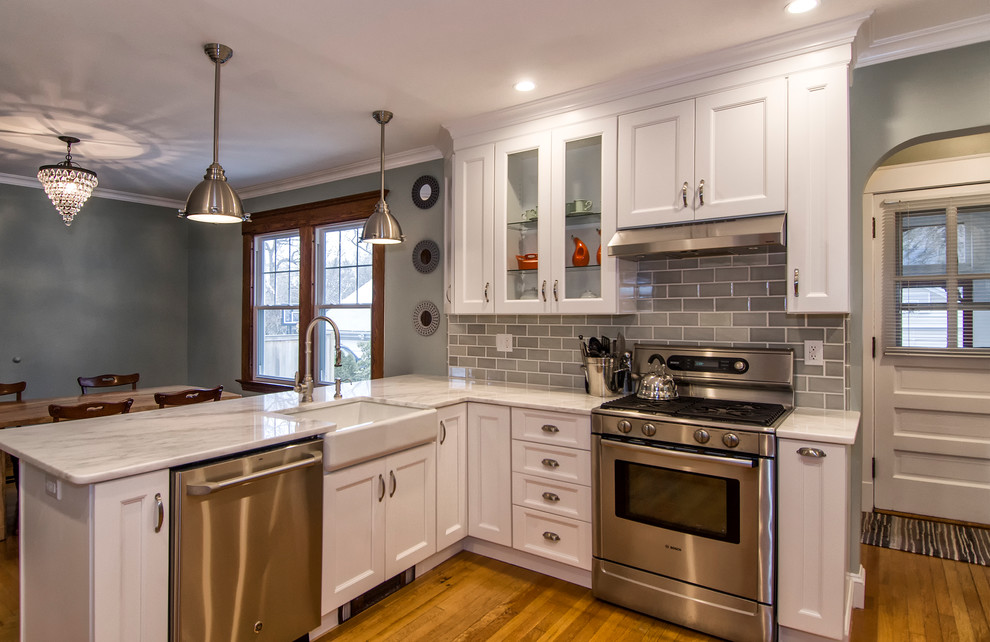 Design ideas for a mid-sized transitional u-shaped eat-in kitchen in Bridgeport with a farmhouse sink, recessed-panel cabinets, white cabinets, marble benchtops, grey splashback, subway tile splashback, stainless steel appliances, medium hardwood floors, a peninsula and brown floor.