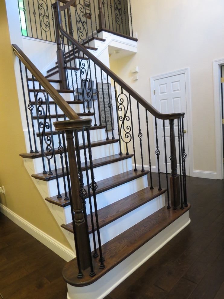 Example of a large transitional galley dark wood floor and brown floor staircase design with a double-bowl sink, raised-panel cabinets, white cabinets, granite countertops, white backsplash, porcelain backsplash, stainless steel appliances and an island
