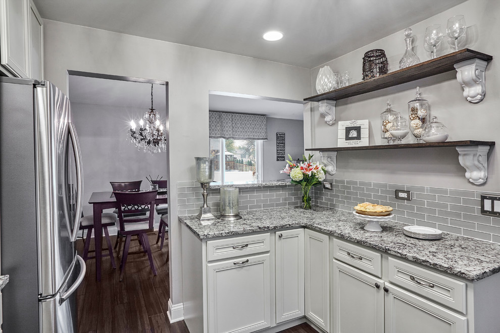 This is an example of a transitional kitchen in Chicago with an undermount sink, recessed-panel cabinets, beige cabinets, granite benchtops, grey splashback, glass tile splashback, stainless steel appliances and bamboo floors.