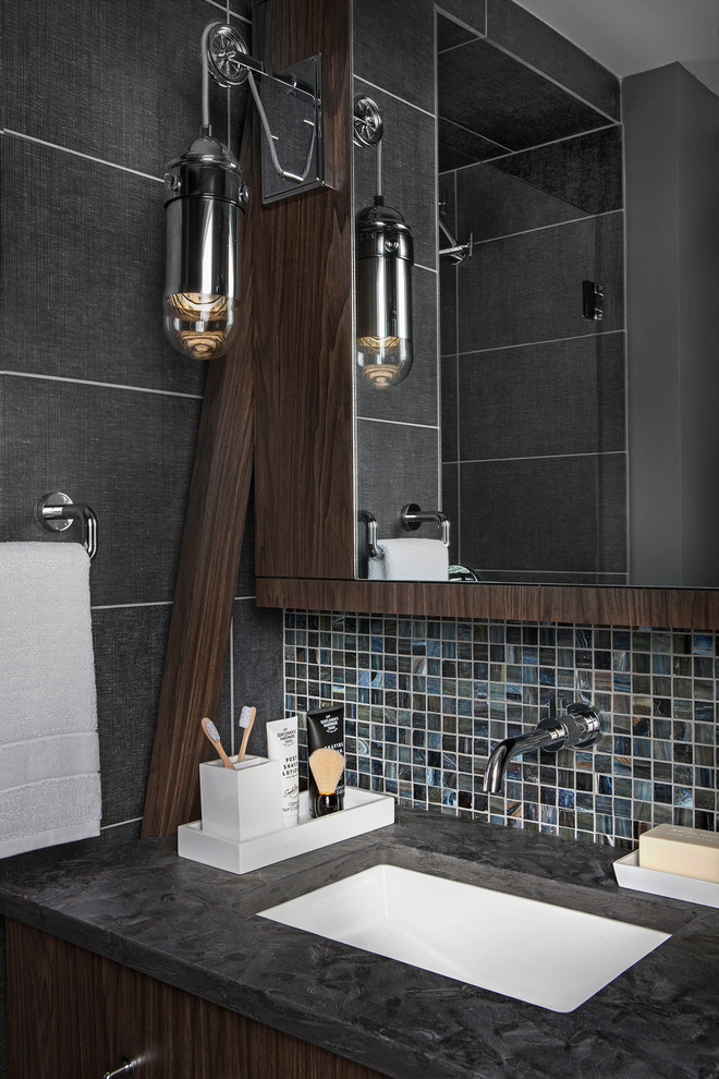 Design ideas for a small industrial 3/4 bathroom in Detroit with flat-panel cabinets, medium wood cabinets, an alcove shower, a wall-mount toilet, blue tile, porcelain tile, blue walls, porcelain floors, an undermount sink, granite benchtops, blue floor, a hinged shower door and black benchtops.