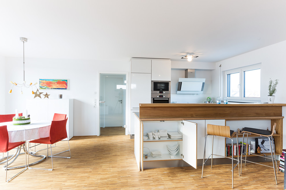 Mid-sized contemporary galley eat-in kitchen in Stuttgart with flat-panel cabinets, white cabinets, laminate benchtops, grey benchtop, an integrated sink, blue splashback, glass sheet splashback, black appliances, medium hardwood floors, a peninsula and brown floor.