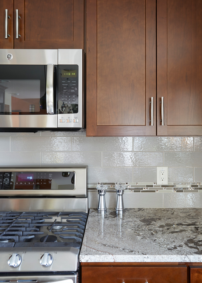 Example of a large transitional l-shaped dark wood floor enclosed kitchen design in Milwaukee with an undermount sink, shaker cabinets, medium tone wood cabinets, granite countertops, white backsplash, porcelain backsplash, stainless steel appliances and an island