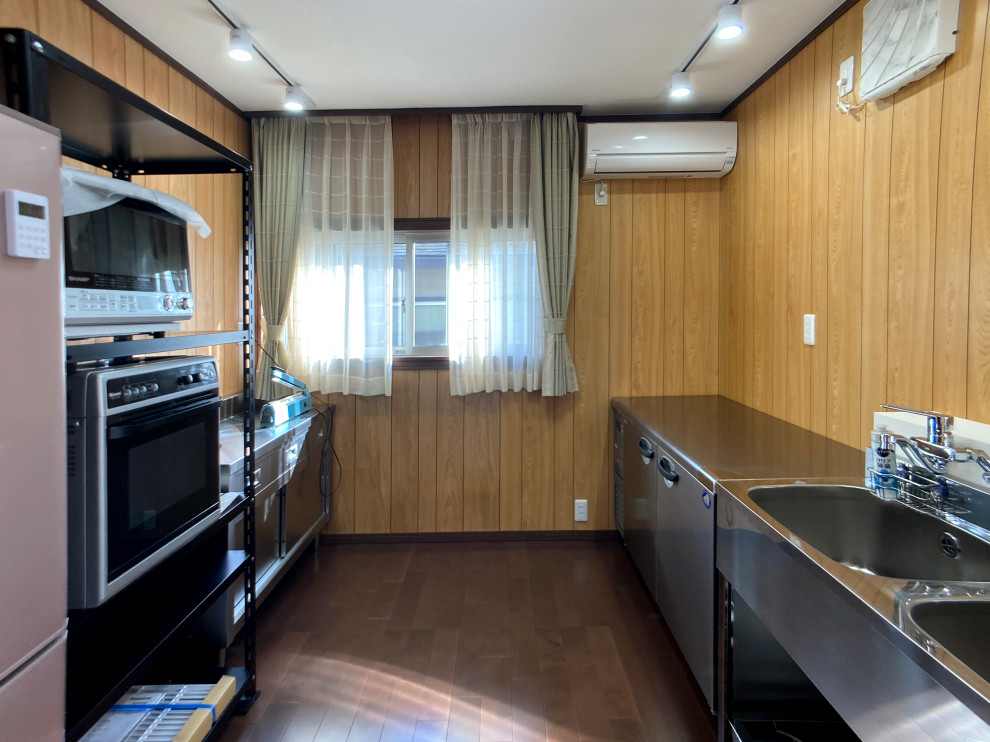 This is an example of a small country galley separate kitchen in Other with an integrated sink, flat-panel cabinets, stainless steel cabinets, stainless steel benchtops, timber splashback, stainless steel appliances, plywood floors, no island, brown floor and wallpaper.