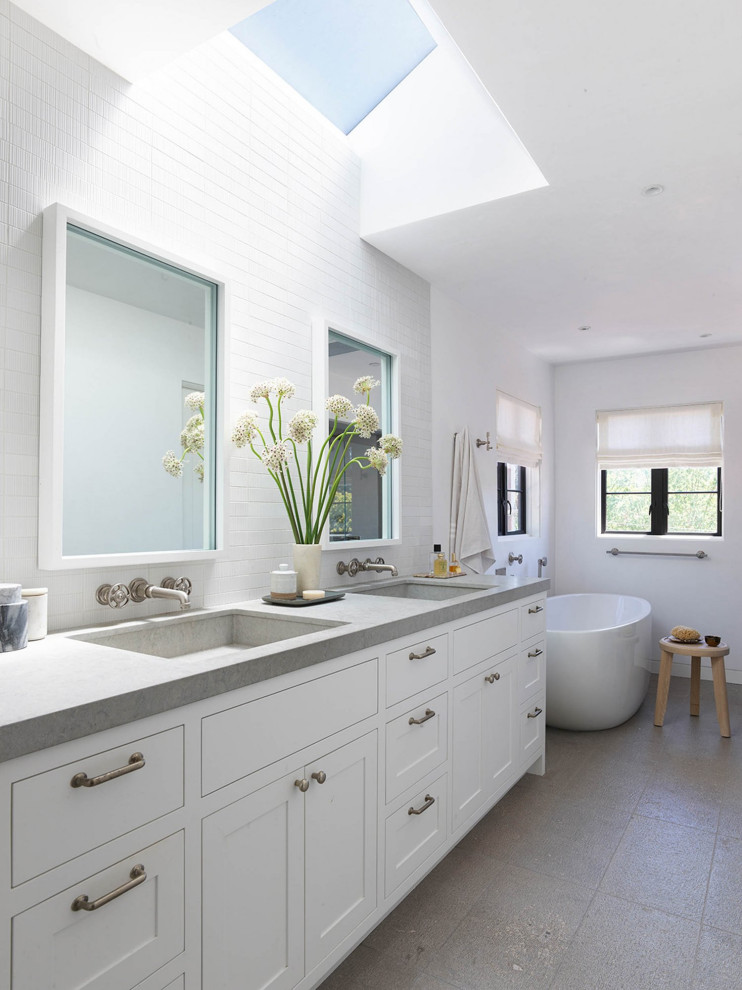 This is an example of a large traditional ensuite bathroom in San Francisco with shaker cabinets, white tiles, white walls, light hardwood flooring, grey worktops, double sinks, a freestanding vanity unit, a freestanding bath, metro tiles, white cabinets, an integrated sink, limestone worktops, grey floors and a vaulted ceiling.