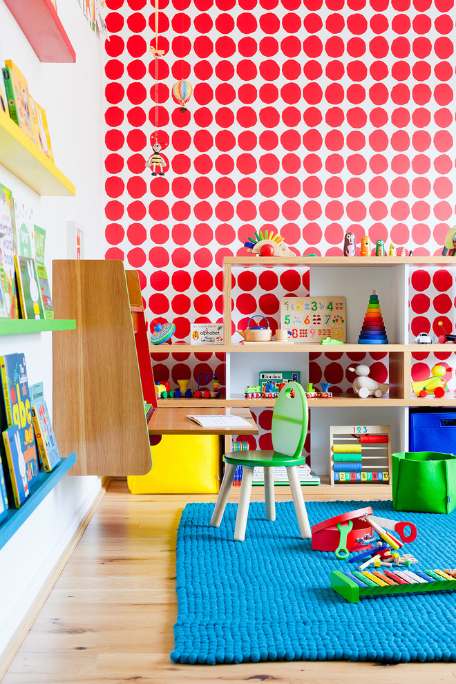 This is an example of a mid-sized contemporary gender-neutral kids' bedroom for kids 4-10 years old in Cambridgeshire with red walls and light hardwood floors.