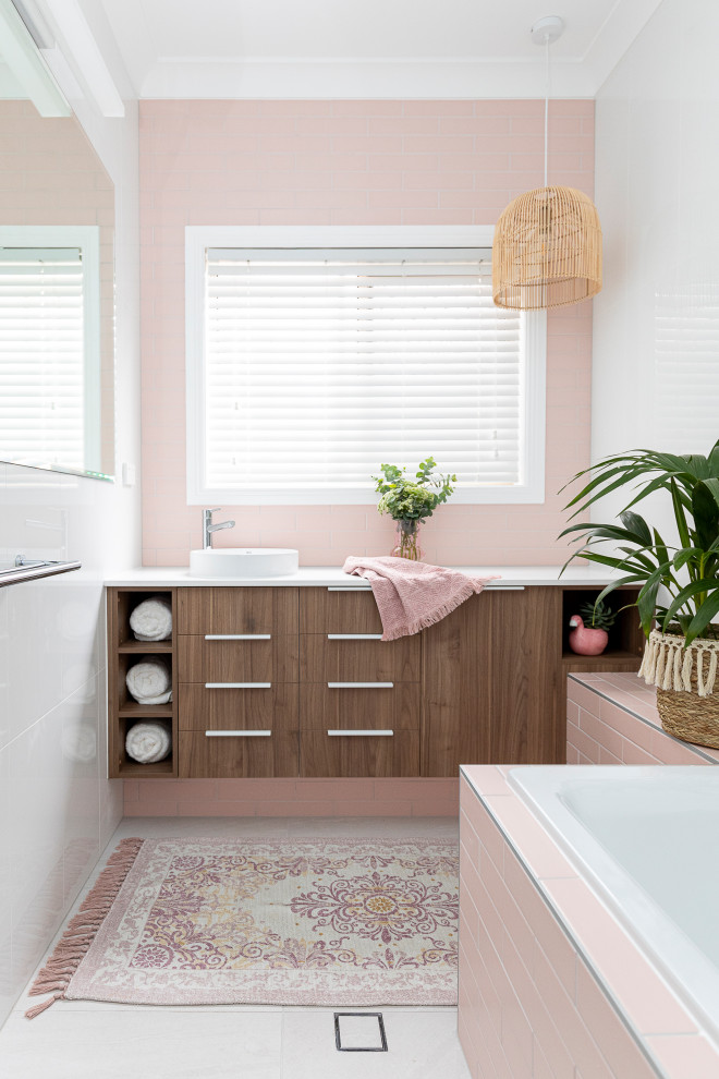 Photo of a small beach style kids bathroom in Brisbane with medium wood cabinets, a drop-in tub, a shower/bathtub combo, pink tile, white walls, grey floor, white benchtops, a single vanity and a built-in vanity.