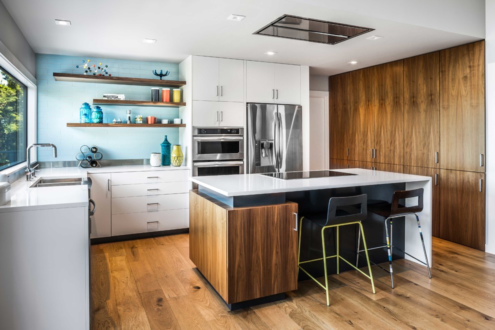 This is an example of a midcentury u-shaped kitchen in Austin with a double-bowl sink, flat-panel cabinets, white cabinets, blue splashback, subway tile splashback, stainless steel appliances, medium hardwood floors and with island.