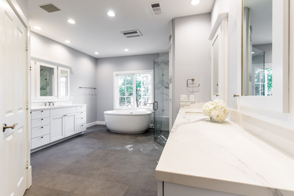 This is an example of a mid-sized contemporary master bathroom in Dallas with white cabinets, a freestanding tub, an open shower, a one-piece toilet, white tile, stone slab, grey walls, an undermount sink, granite benchtops, grey floor, an open shower, white benchtops, an enclosed toilet and a double vanity.
