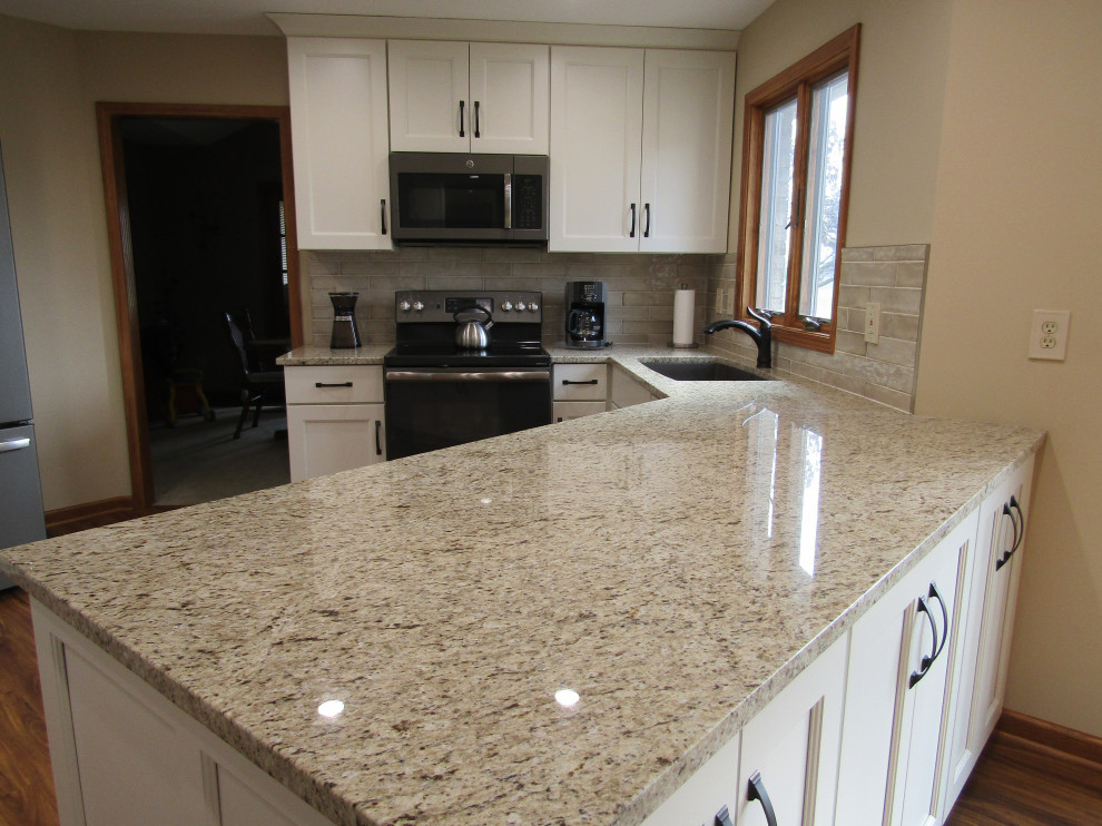 This is an example of a traditional eat-in kitchen in Indianapolis with an undermount sink, recessed-panel cabinets, white cabinets, granite benchtops, beige splashback, ceramic splashback, medium hardwood floors, brown floor and brown benchtop.