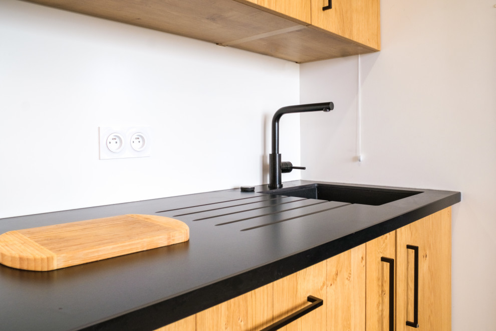 Diseño de cocina lineal moderna de tamaño medio abierta sin isla con puertas de armario de madera clara, electrodomésticos negros, encimeras negras y fregadero integrado