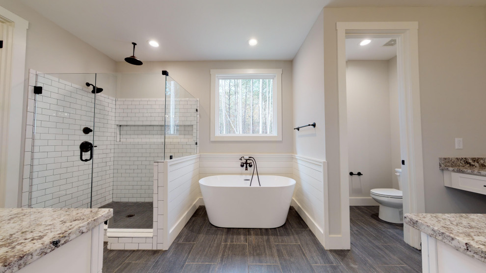 This is an example of a large country master bathroom in Atlanta with shaker cabinets, white cabinets, a freestanding tub, a corner shower, a two-piece toilet, white tile, subway tile, grey walls, ceramic floors, an undermount sink, granite benchtops, grey floor, a hinged shower door and multi-coloured benchtops.