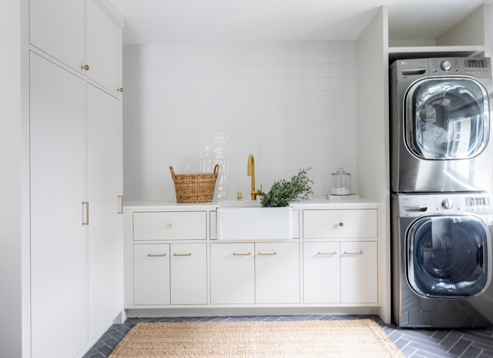 Design ideas for a mid-sized scandinavian l-shaped dedicated laundry room in Vancouver with a farmhouse sink, white cabinets, white splashback, white walls, a stacked washer and dryer, grey floor and white benchtop.