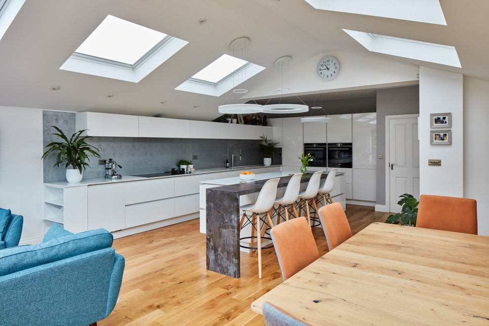 Design ideas for a large modern galley kitchen/diner in London with a built-in sink, flat-panel cabinets, white cabinets, granite worktops, grey splashback, metal splashback, integrated appliances, dark hardwood flooring, an island, brown floors and white worktops.