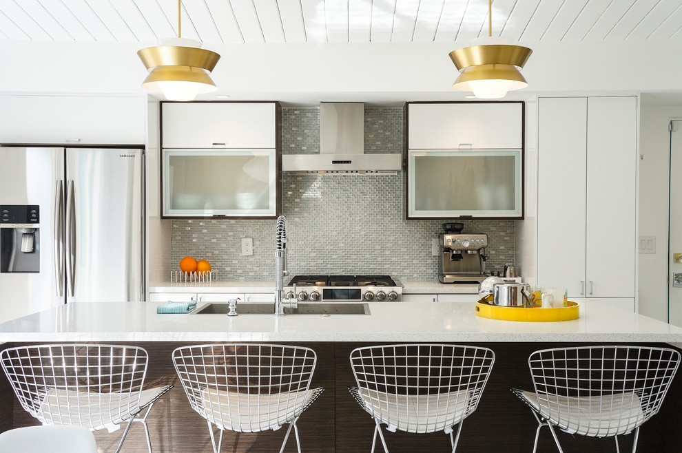 Photo of a midcentury galley kitchen in Other with a drop-in sink, flat-panel cabinets, white cabinets, grey splashback, matchstick tile splashback, stainless steel appliances, with island and white benchtop.