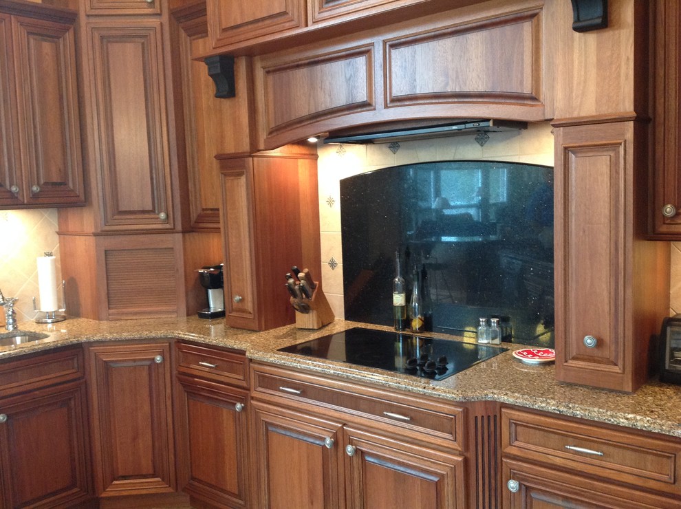 Eat-in kitchen - eat-in kitchen idea with raised-panel cabinets, brown cabinets, granite countertops, white backsplash, black appliances, an island and an undermount sink