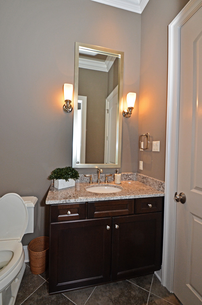 Mid-sized traditional powder room in New Orleans with an undermount sink, recessed-panel cabinets, dark wood cabinets, a one-piece toilet, gray tile and grey walls.