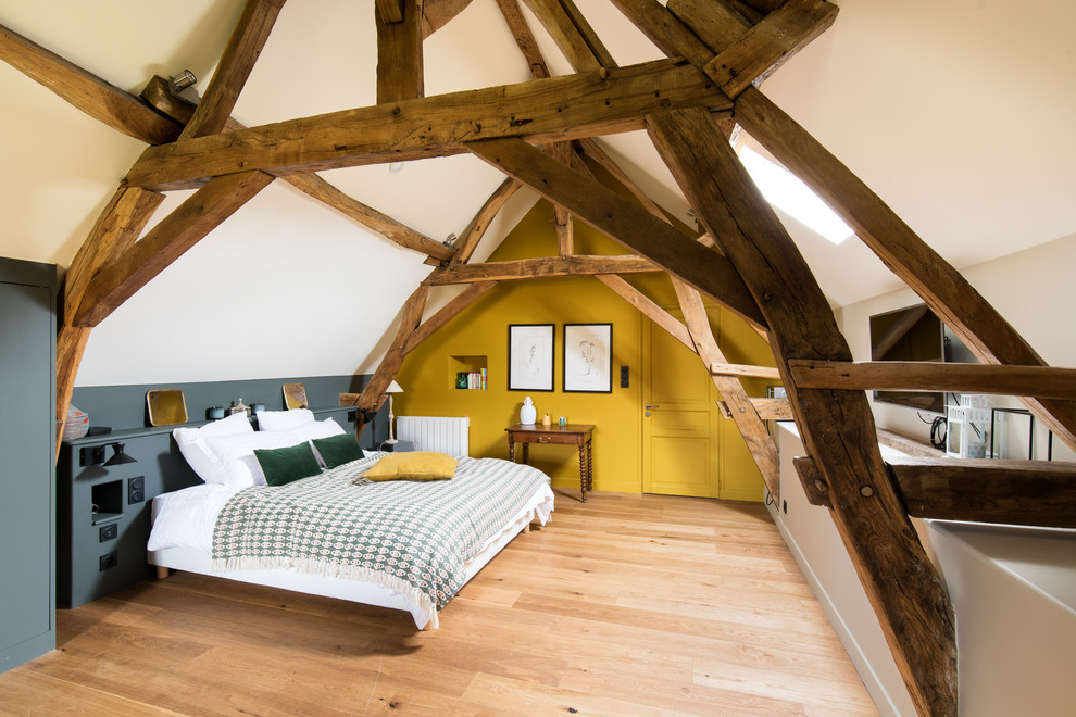 Country bedroom in Paris with yellow walls, light hardwood floors and beige floor.
