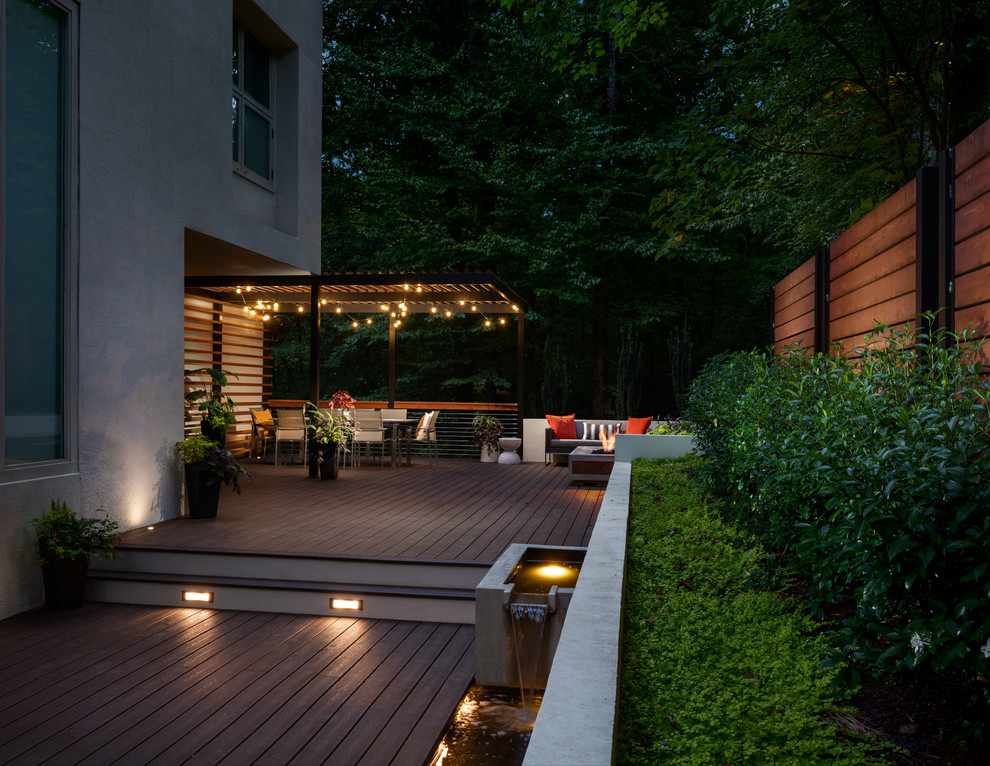 This is an example of a large contemporary backyard and ground level deck in Atlanta with a fire feature, a pergola and metal railing.
