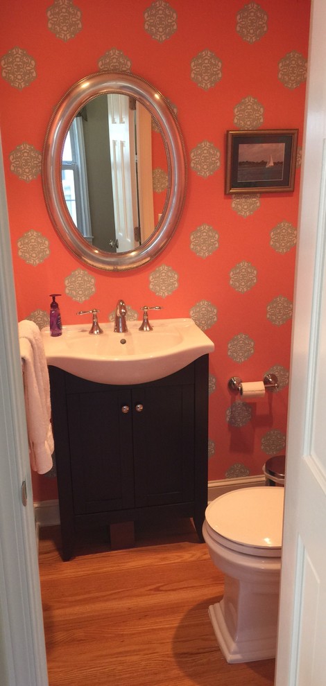 Mid-sized transitional powder room in New York with shaker cabinets, dark wood cabinets, a two-piece toilet, orange walls and an integrated sink.