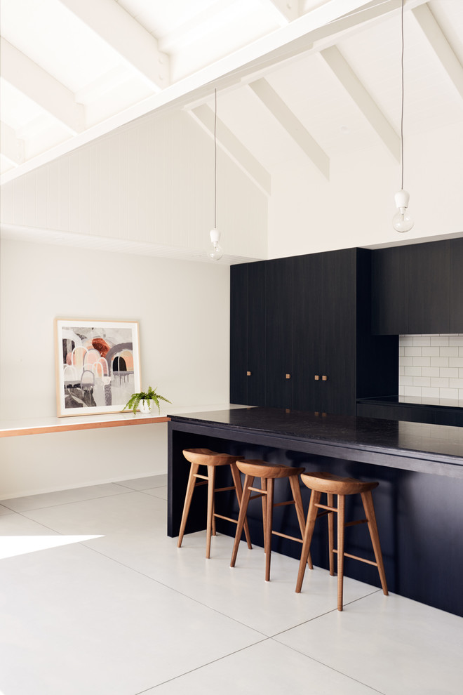 Photo of a contemporary galley kitchen in Melbourne with flat-panel cabinets, white splashback, subway tile splashback, with island, white floor and black benchtop.