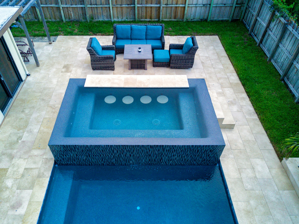 Design ideas for a mid-sized modern backyard custom-shaped infinity pool in Miami with a hot tub and natural stone pavers.