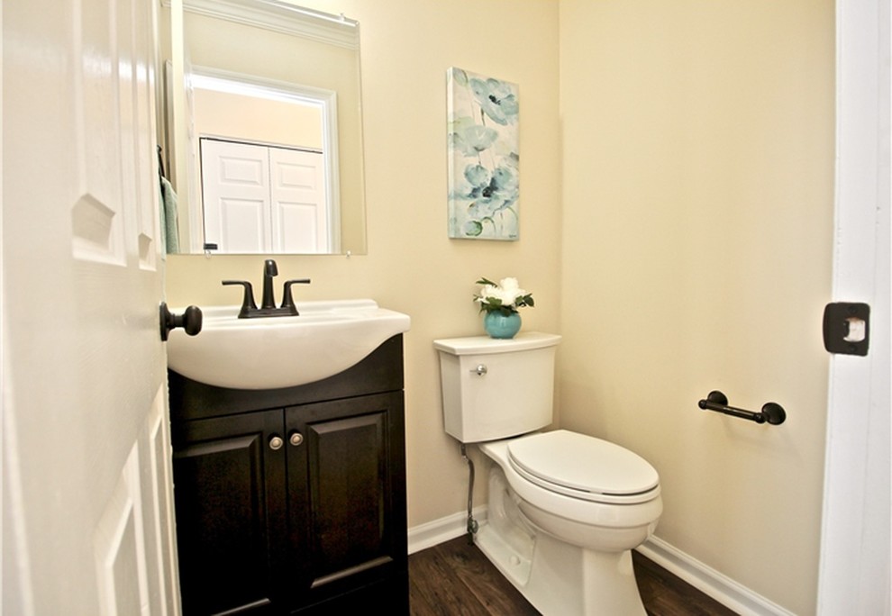 Photo of a small traditional powder room in Other with raised-panel cabinets, brown cabinets, a two-piece toilet, beige tile, beige walls, laminate floors, a console sink, marble benchtops, brown floor and white benchtops.