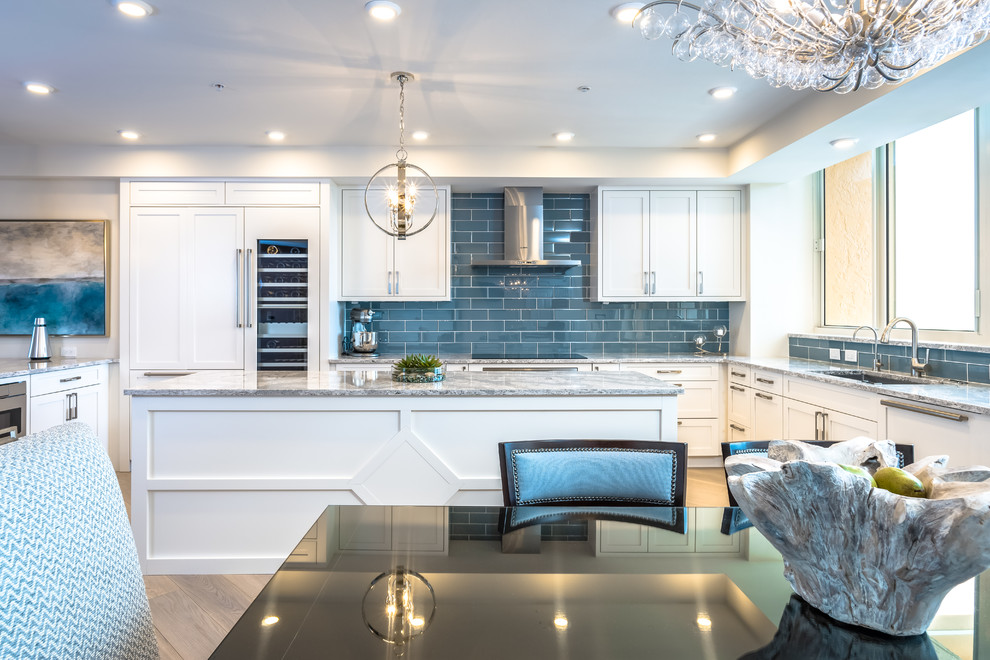 Photo of an expansive transitional u-shaped eat-in kitchen in Miami with a drop-in sink, shaker cabinets, white cabinets, granite benchtops, blue splashback, subway tile splashback, panelled appliances, light hardwood floors and multiple islands.