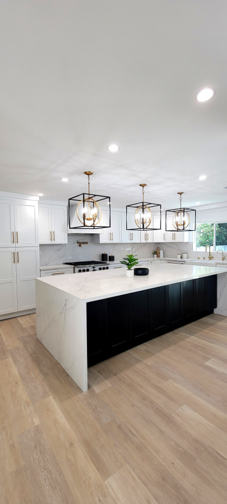 Large modern l-shaped open plan kitchen in Los Angeles with a farmhouse sink, shaker cabinets, white cabinets, quartz benchtops, white splashback, engineered quartz splashback, white appliances, vinyl floors, with island, brown floor and white benchtop.