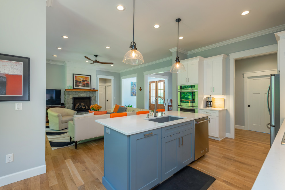 Example of a mid-sized transitional l-shaped light wood floor and brown floor kitchen design with an undermount sink, shaker cabinets, white cabinets, quartzite countertops, white backsplash, ceramic backsplash, stainless steel appliances, an island and white countertops