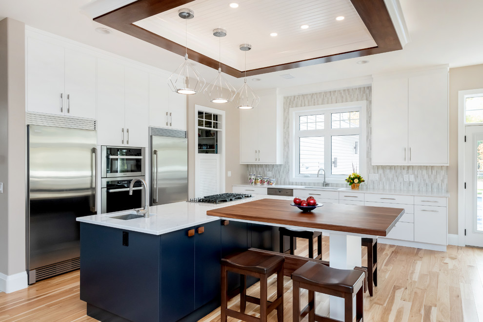 Example of a large transitional l-shaped light wood floor and beige floor kitchen pantry design with a double-bowl sink, flat-panel cabinets, white cabinets, quartz countertops, gray backsplash, cement tile backsplash, stainless steel appliances, an island and white countertops