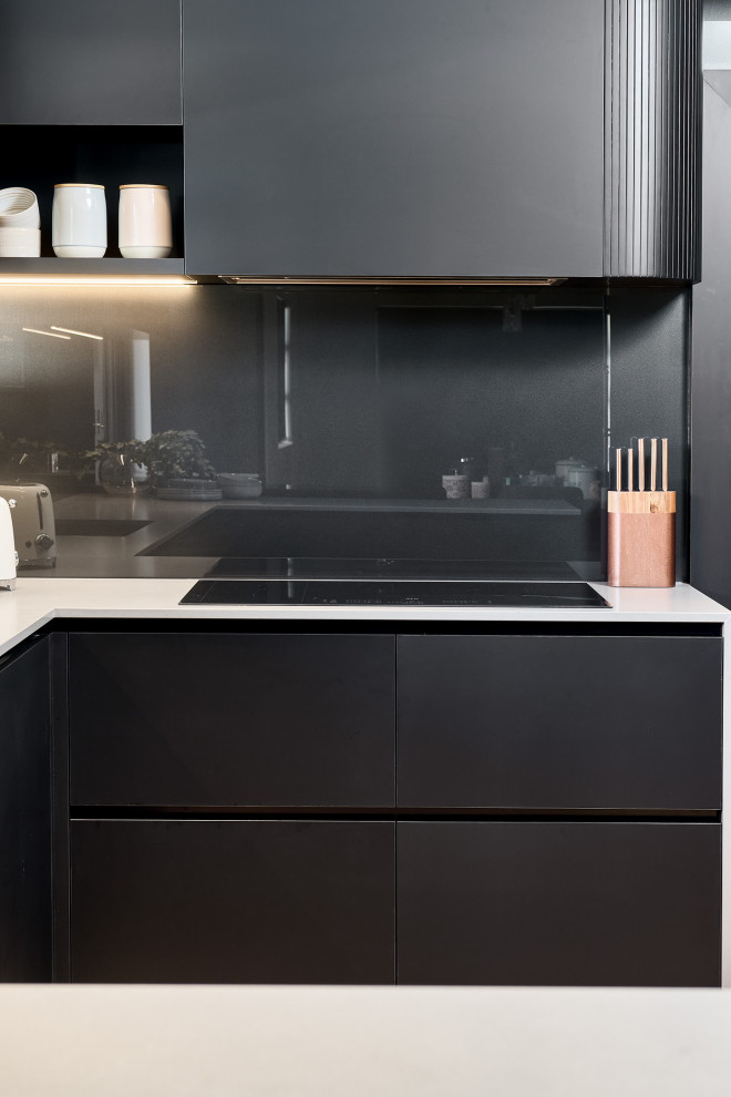 Inspiration for a large contemporary u-shaped open plan kitchen in Perth with an undermount sink, flat-panel cabinets, black cabinets, quartz benchtops, black splashback, glass sheet splashback, black appliances, light hardwood floors, with island, brown floor, grey benchtop and recessed.