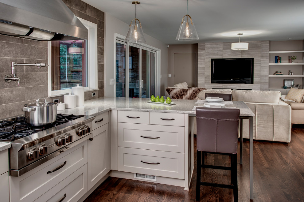 Design ideas for a large transitional l-shaped eat-in kitchen in Seattle with an undermount sink, recessed-panel cabinets, white cabinets, quartz benchtops, grey splashback, porcelain splashback, stainless steel appliances, medium hardwood floors, red floor and grey benchtop.