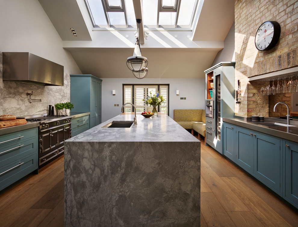 Design ideas for a large transitional u-shaped separate kitchen in London with an undermount sink, recessed-panel cabinets, blue cabinets, solid surface benchtops, grey splashback, stone slab splashback, stainless steel appliances, medium hardwood floors, with island and brown floor.