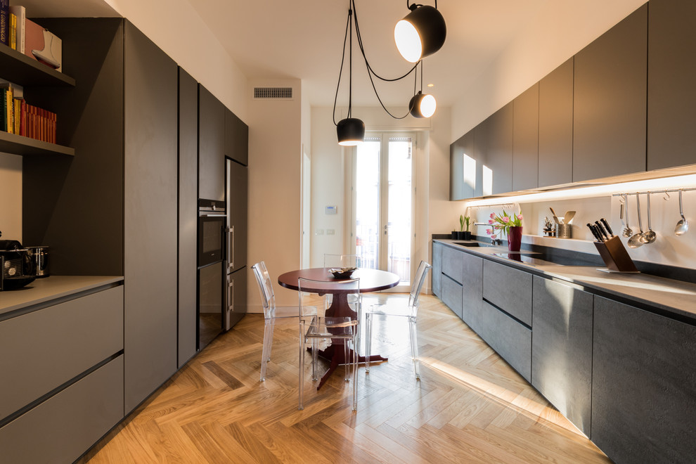 Photo of a mid-sized contemporary galley separate kitchen in Milan with grey cabinets, no island, flat-panel cabinets, stainless steel appliances, medium hardwood floors, brown floor, an integrated sink and concrete benchtops.