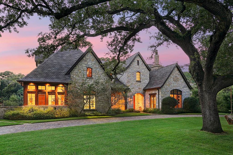 Photo of a large traditional two-storey grey exterior in Houston with stone veneer and a gable roof.