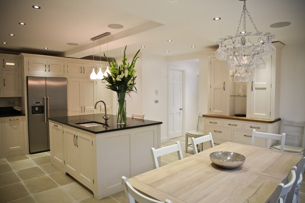 This is an example of a large transitional l-shaped eat-in kitchen in London with an undermount sink, shaker cabinets, white cabinets, granite benchtops, black splashback, glass sheet splashback, stainless steel appliances, limestone floors and with island.
